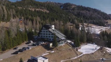 Dolomitler 'de, kar yamaçları, yemyeşil ormanlar ve engebeli dağ zirveleriyle çevrili lüks bir otelin yavaş yavaş havalanan görüntüsü..