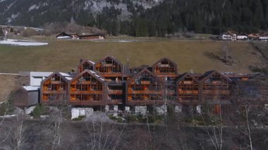 Dolomitler 'de lüks bir otelin havadan görünüşü. Alp tarzı ahşap cepheler, çimenli yamaçlar, ormanlar ve dağınık yamaçlardaki evler..