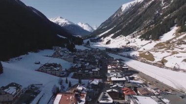 Avusturya Alplerinde Ischgl 'in hava görüntüsü, karla kaplı çatılar, kayak yamaçları, teleferik sistemi ve çevresindeki dağlık orman ve tepeleri gösteriyor..