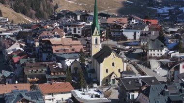 Ischgl, Avusturya 'nın havadan görünüşü, yeşil kule, Chalets, oteller, kar bantları ve KIWI etiketli bir bina içeren sarı bir kilise..