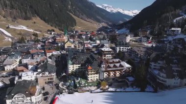 Ischgl, Avusturya 'nın havadan görünüşü, yeşil çatılı bir kilise, lüks bir otel, park alanı ve kar ile kaplı yamaçlar.