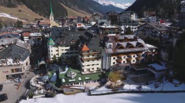 Ischgl, Avusturya 'nın havadan görünüşü, lüks oteller, yeşil sarmal bir kilise, karla kaplı dağlar, kayak asansörleri ve yavaş hareket eden bir tava..