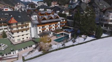 Ischgl, Avusturya 'nın havalimanı, lüks bir otel, yeşil çatılı kilise, karla kaplı zemin, açık havuz ve arka planda dağları gösteriyor..