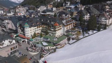 Avusturya 'nın Ischgl kentinin havadan görünüşü, yeşil kulesi, lüks otelleri, açık hava aktiviteleri ve dağlarla kaplı dağları olan bir kiliseyi gösteriyor..