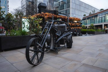 Modern cam binalar, yeşillik ve sonbahar yaprakları ile çevrili Londra plazasında steampunk tasarımlı sanatsal metal motosiklet heykeli..