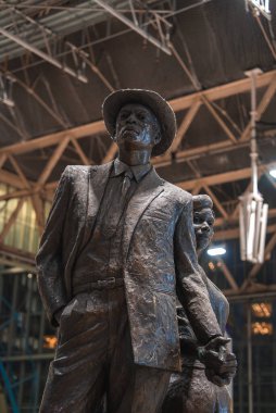Londra 'daki Waterloo tren istasyonunda çelik ve cam bir yapıya karşı kapalı bir yerde duran takım elbiseli ve şapkalı bir adamın bronz heykeli..