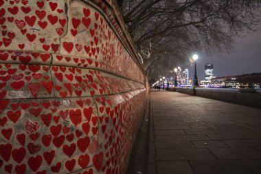 Londra 'daki Ulusal Covid Anıt Duvarı' nda kırmızı el boyalı kalpler, sokak lambaları, çıplak ağaçlar ve Thames Nehri 'nin yanındaki ufuk çizgisi vardı..