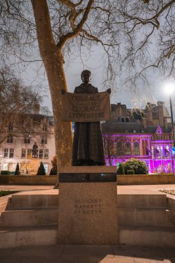 Millicent Garrett Fawcett heykeli Parlamento Meydanı, Londra 'da, geceleri, sokak lambaları, renkli bina ışıkları ve arka planda çıplak ağaçlarla.