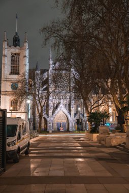 Londra 'daki Westminster Manastırı' nın aydınlık cephesi, çıplak ağaçlarla çevrili. Asfalt kaldırımda beyaz bir minibüs park halinde, çok az hareketlilik var..