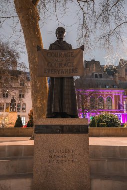 Millicent Garrett Fawcett 'in Londra Parlamento Meydanı' ndaki heykeli. Mor renkli binalar, bir ağaç ve manzaralı başka bir heykel..