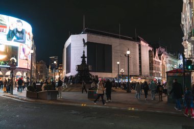 Londra 'daki Piccadilly Sirki' nin gece manzarasında Shaftesbury Memorial Fountain, dijital reklam panoları, aydınlık binalar ve toplanan insanlar.