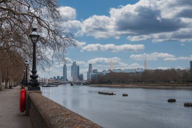 Londra 'daki Thames Nehri manzarasında Battersea Enerji İstasyonu, modern gökdelenler, nehir kenarında bir yürüyüş yolu ve çıplak kış ağaçları yer alıyor..