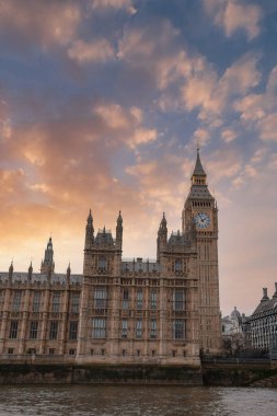 Elizabeth Tower, Westminster Sarayı 'nın bir parçası, turuncu ve pembe renklerle gün batımına karşı duruyor. Thames Nehri yumuşak akşam ışığını yansıtır..