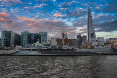 Londra 'nın gökdelenli ufuk çizgisi Thames nehri üzerindeki HMS Belfast ve bulutlu gökyüzü altındaki modern cam binalar..
