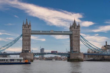 Londra, İngiltere 'deki Tower Bridge, ikonik kuleleri ve üst yürüyüş yolları, kırmızı çift katlı otobüs geçişi, ve ön planda rıhtımda bir tekne.