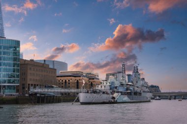 HMS Belfast, The Shard ve şehir mimarisi tarafından çerçevelenen Thames Nehri 'ne demirledi. Pembe ve turuncu renkli canlı bir günbatımı sahneyi aydınlatıyor..