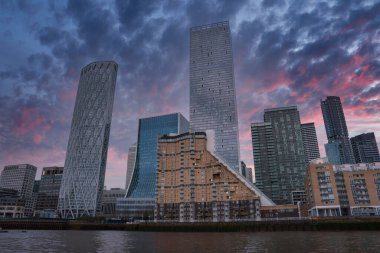 Newfoundland Quay ve Landmark Pinnacle gökdelenlerinin yer aldığı modern Londra gökdelenleri Thames Nehri boyunca pembe ve mor gün batımı gökyüzünün altında.