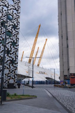 O2 Arena 'nın beyaz kubbesi ve sarı direkleri modern binaların arasında göze çarpıyor. Buna, bulutlu Londra semaları altında geometrik bir cephe de dahil..