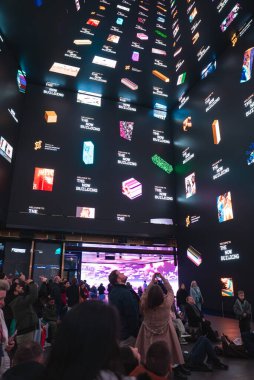 Londra 'daki Now Building Outernet' te canlı görselleri ve metni olan yüksek dijital ekranlar yer alıyor. İnsanlar toplanıyor, bazıları resimlerini çekiyor..