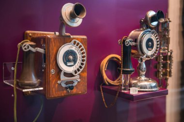 Krank kolu olan ahşap bir telefon ve süslü detaylarıyla cilalanmış metalik bir telefon sergileniyor..