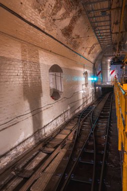 Eski tuğla duvarlar ve çift raylı raylar Londra 'daki bir yeraltı tüneline doğru kıvrılıyor. Tepedeki borular ve metal yürüyüş yolu endüstriyel detay ekler..