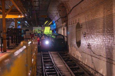 Londra, İngiltere 'de az aydınlatılmış yeraltı posta tüneli, tuğla duvarlar, raylar, yeşil tren vagonları, sarı korkuluklar ve endüstriyel detaylar.
