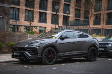 Siyah jantlı, kırmızı fren ayarlı gri bir Lamborghini Urus Londra 'daki modern tuğlalı bir binanın önünde park halinde..