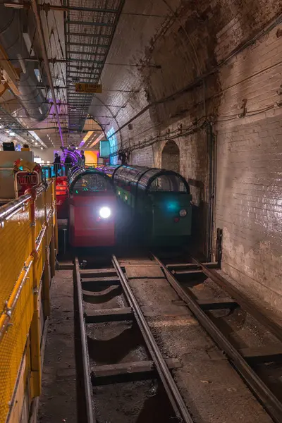 Londra Posta Müzesi 'nin raylarda kırmızı ve yeşil trenler, kemerli tuğla duvarlar ve modern ışıklandırmanın yer altı görüntüsü.