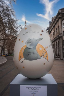 Londra mimarisi ve arka planda saat kulesi olan hilal altında bir filin yer aldığı açık havada yumurta heykeli..