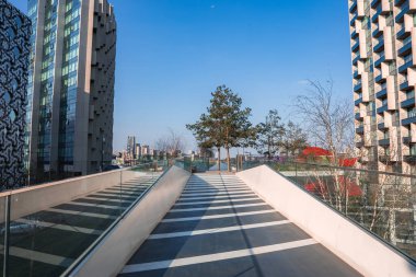 Londra 'da açık mavi gökyüzünün altında eşsiz cepheleri olan yüksek binalarla çevrili, ağaçlara ve açık bir alana açılan cam raylı bir yol..