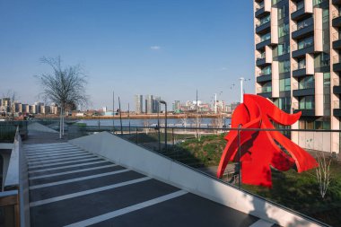 Londra 'da kırmızı soyut bir heykel, yaya geçidi, yüksek binalar ve nehir üzerinde Emirates Hava Hattı teleferiklerinin yer aldığı şehir merkezi..