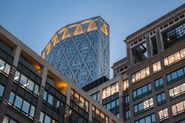 Londra 'daki 22 Bishopsgate' in akşam manzarası aydınlık elmas desenli cepheleriyle aydınlık bir gökyüzü altında ofis binalarıyla çevrili..
