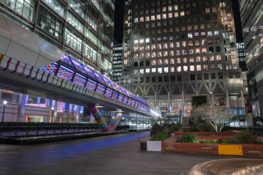 Geceleri Canary Wharf 'ta modern mimari, renkli bir geometrik yaya köprüsü, peyzajlı ekiciler, çiçekler ve küçük bir ağaç bulunur..