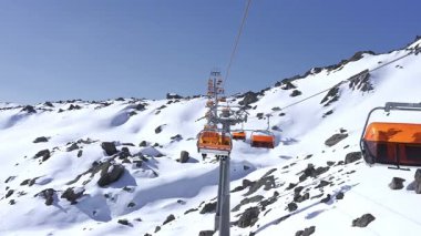 Parlak turuncu kayak kaldırma koltukları Zermatt 'taki karlı arazide durmadan hareket eder. Sert kar manzarası ve kayak kaldırma altyapısı görülebiliyor.