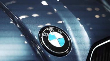 BMW logosu parlak metalik mavi bir yüzeye yakın plan çekilmiş. Statik çekim yansıtıcı kapanışı ve lüks işçiliği vurguluyor.