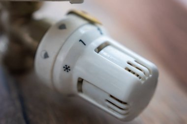 Beyaz bir döner ısıtma düğmesinin yakın görüntüsü numaralandırılmış ayarlar ve bir kar tanesi simgesi, muhtemelen bir su ya da ısıtma kontrol sisteminin parçası. Bulanık tahta arkaplan.