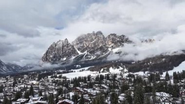 Cortina ve Ampezzo 'nun karla kaplı çatıları, sık ormanları ve kayan bulutlarla kısmen örtülü Dolomitlerin zirveleri..