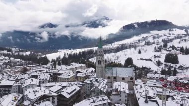 Bazilika Minore çan kulesi, dağlık binalar, karlı yamaçlar, yoğun ormanlar ve sisli dağ tepeleriyle Cortina dAmpezzo 'nun hava manzarası..