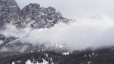 Cortina yakınlarındaki engebeli Dolomite tepeleri, karla kaplı yamaçlar, seyrek ağaçlar, ve yavaş ve sisli bulutlar..