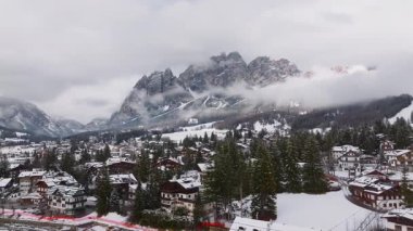 Cortina ve Ampezzo 'nun karla kaplı çatıları, Bazilika Minore çan kulesi ve alçak bulutların altında dramatik Dolomite zirveleri..