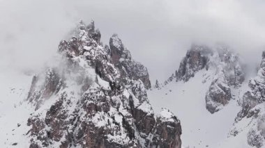 Uçsuz bucaksız, karla kaplı Dolomite tepeleri Cortina yakınlarında, sis ve bulutlar uçurumların ve dağınık yeşil ağaçların üzerinde sürükleniyor..