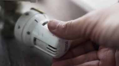 1 'den 5' e kadar olan bir radyatörün beyaz ısıtma düğmesine yakın çekim görüntüsü, döndürülürken hareketi gösteriyor. Ahşap zemin ve arka plandaki duvar..