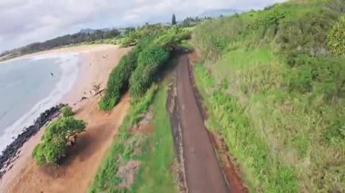 Islak kumlara yayılan dalgaların, yemyeşil çimlerin, dağınık ağaçların ve Oahu veya Kauai 'de parçalı bulutlu bir gökyüzünün olduğu sakin sahil manzarası..