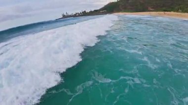 Yumuşak dalgalı turkuaz okyanus suları, kumlu bir sahil, yemyeşil tepeler ve tropik Hawaii 'de beyaz bir kule manzarası..