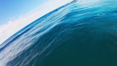 Dinamik turkuaz dalgalar, parlak mavi gökyüzünün altında kayalık bir Hawaii sahil şeridine çarpar ve köpük oluşturur..