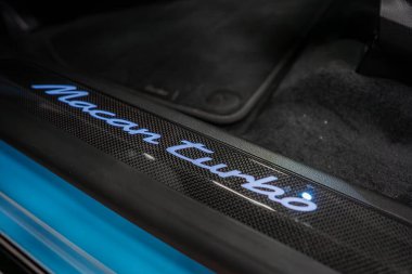 Karbon fiber kapı pervazındaki parlak Macan Turbo logosunu kapat, Porsche Macan Turbo iç döşemesi içinde koyu renk halılarla çevrili..