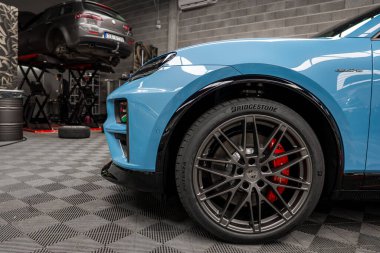 Kırmızı fren kalibreli ve Bridgestone lastikli mavi bir Lamborghini Urus 'un ön bölümü, bir otomotiv atölyesinde kareli bir zemine park edilmiş..