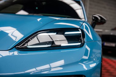 Mavi bir Porsche Macan farının detaylı bir görüntüsü, muhtemelen bir Porsche Macan, yansıtıcı ışıklandırması ve arka planda bulanık bir tuğla duvarı olan bir ev..