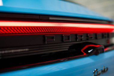 Aydınlatılmış kırmızı LED stop lambası, siyah Porsche harfi ve kısmen görünür gümüş Turbo rozet gösteren mavi bir Porsche 'nin arka görüntüsü..