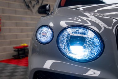 Bentley Bentayga 'nın ön far montajı. Aydınlatılmış mavi LED ışıklar, gri dış döşeme, sergi salonunda tuğla bir duvar..